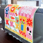 Colorful quilt with 'Hello Spring' text draped over a sofa in a living room.