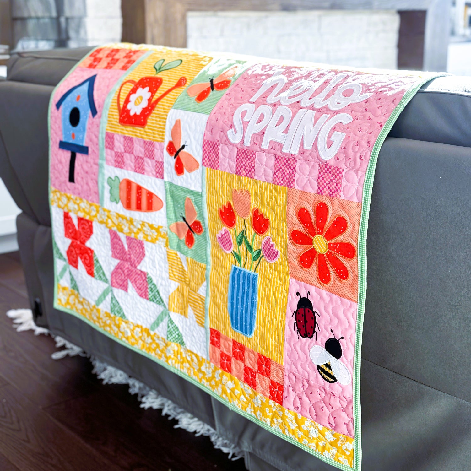 Colorful quilt with 'Hello Spring' text draped over a sofa in a living room.