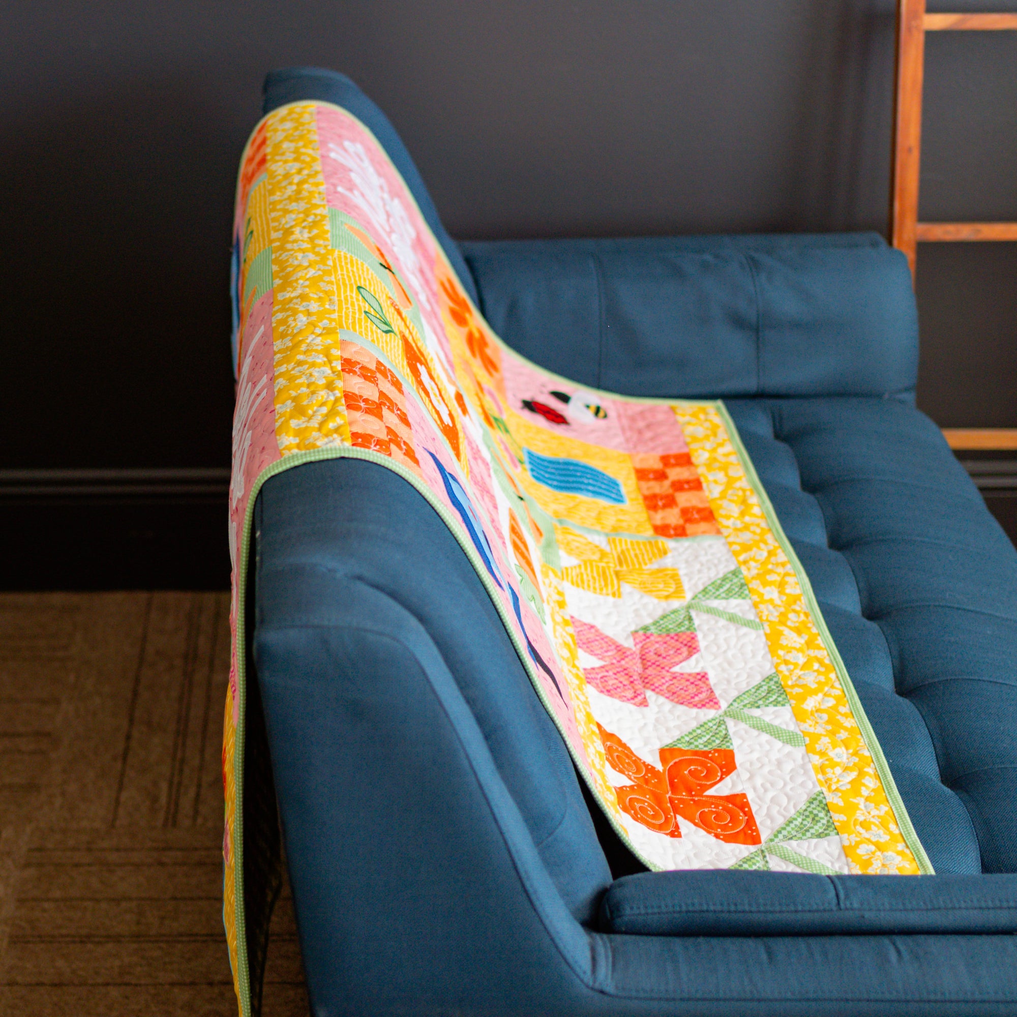 Colorful quilt draped over a blue sofa against a dark wall.