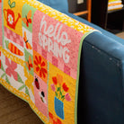 Colorful quilt with 'hello SPRING' text draped over a blue couch.