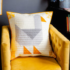 Decorative goose pillow with geometric pattern on a yellow armchair against a dark wall.