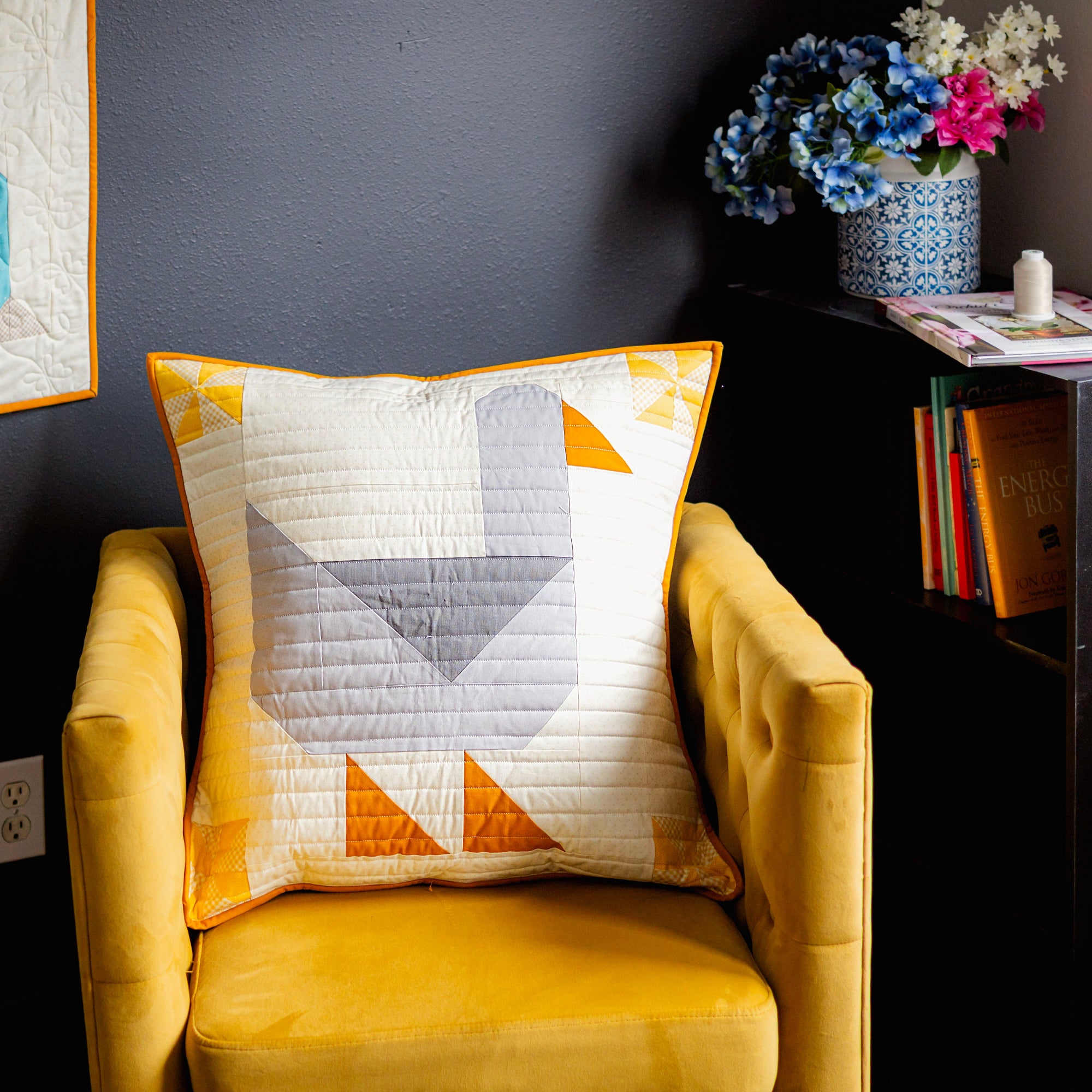 Yellow armchair with a geometric-patterned goose pillow against a dark wall.