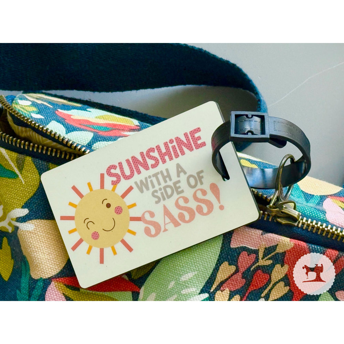 Colorful bag with a humorous luggage tag reading 'Sunshine with a Side of Sass' on a neutral background.