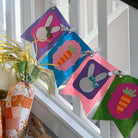 Colorful Easter-themed fabric banner hanging on a window sill with decorative eggs and a teddy bear.
