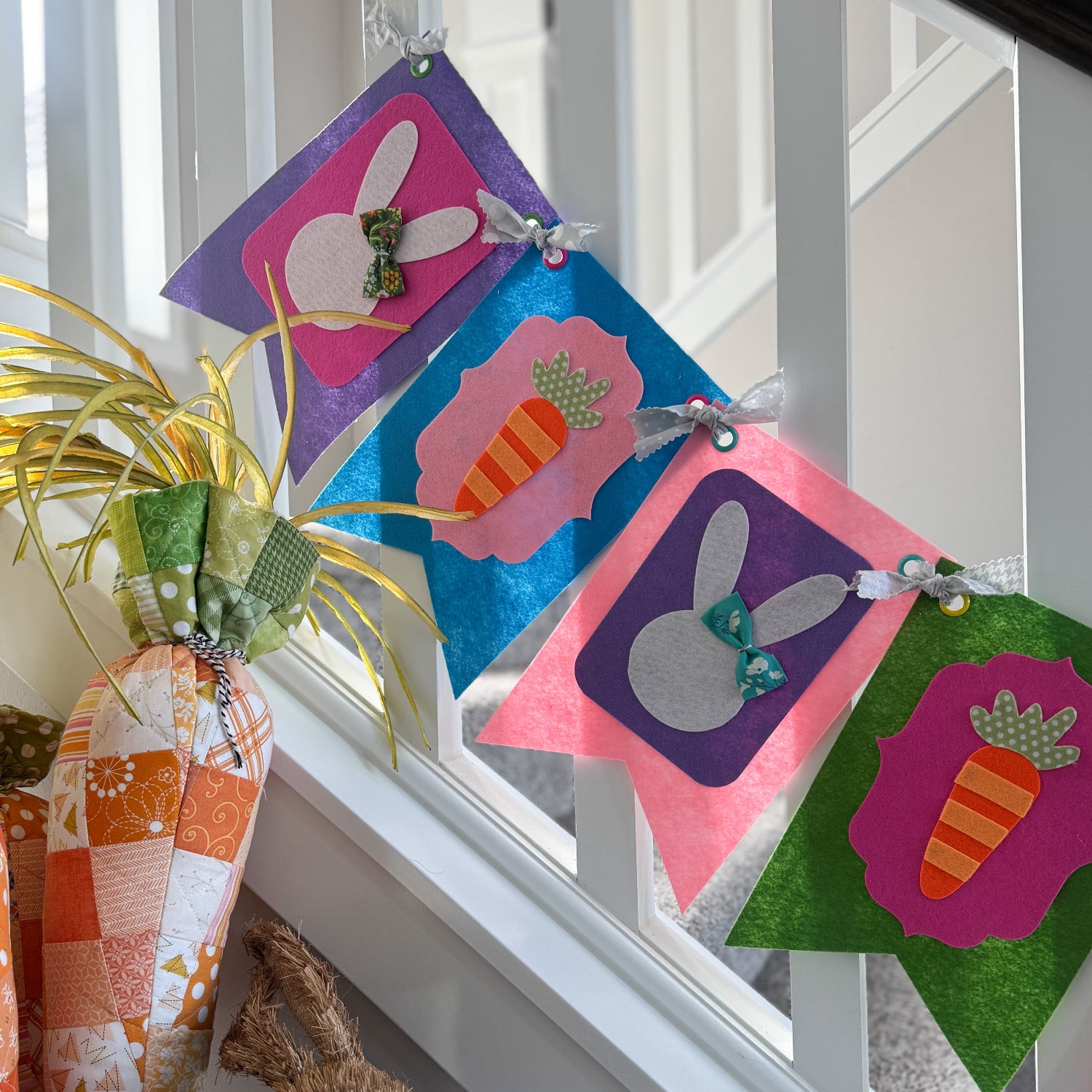 Colorful Easter-themed fabric banner hanging on a window sill with decorative eggs and a teddy bear.