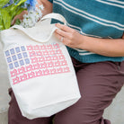 Person holding a tote bag with a pattern, wearing a blue sweater and brown pants.