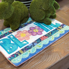 Two green moss-covered bunny figurines on a colorful fabric with floral patterns and letters.
