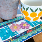 Colorful mug with floral design on a matching coaster on a wooden surface.