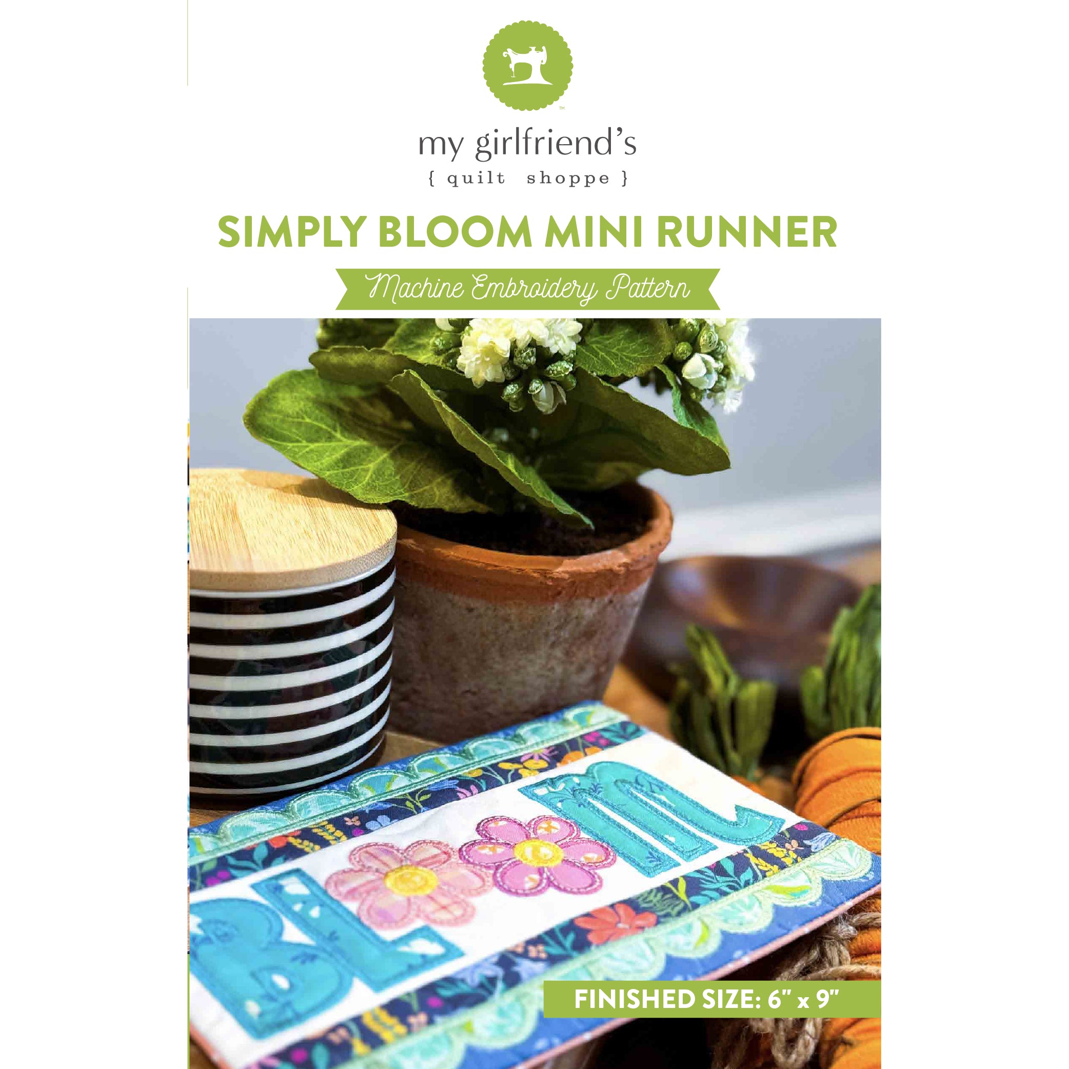Embroidery pattern book titled 'Simply Bloom Mini Runner' with a potted plant and striped cup in the background.