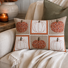 A rectangular decorative throw pillow with a patchwork pumpkin design, styled on a beige couch with a cream knit blanket and a green pillow in a cozy home setting.