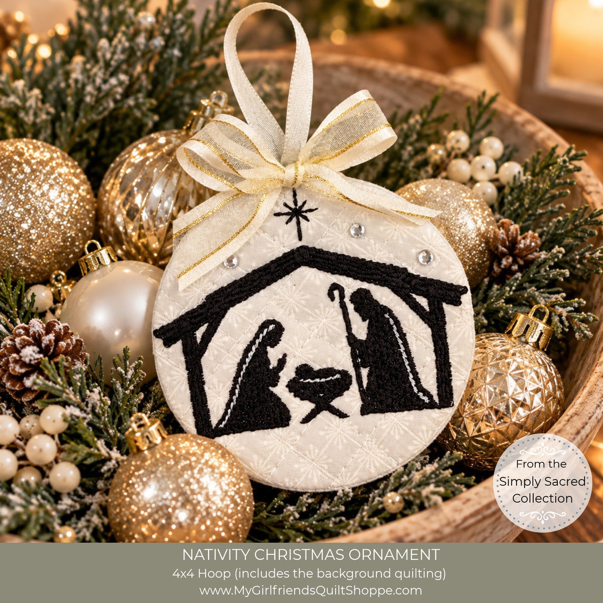 A round white fabric Christmas ornament with a black embroidered nativity scene and a cream ribbon bow, displayed in a decorative holiday arrangement with gold and white ornaments, pinecones, and greenery. Text at the bottom reads 'NATIVITY CHRISTMAS ORNAMENT' and includes the website MyGirlfriendsQuiltShoppe.