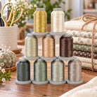 Nine spools of thread in assorted colors and textures, stacked in a pyramid on a wooden table with sewing-themed props like scissors, fabric, and decorative pumpkins.