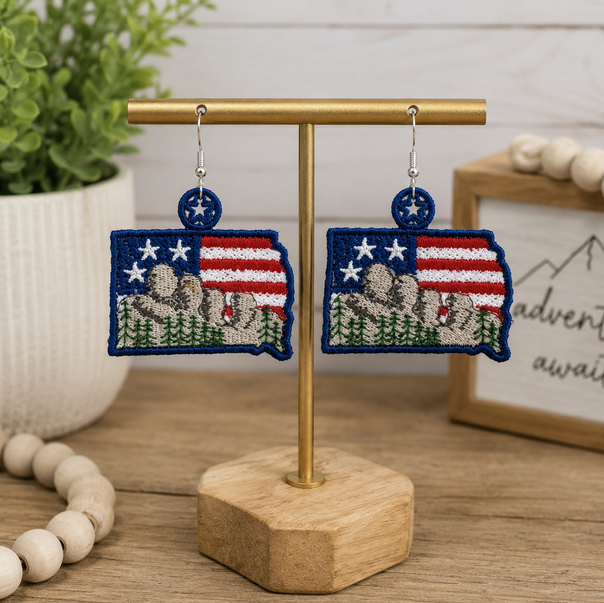 Pair of earrings with American flag design on a gold stand with a wooden base.