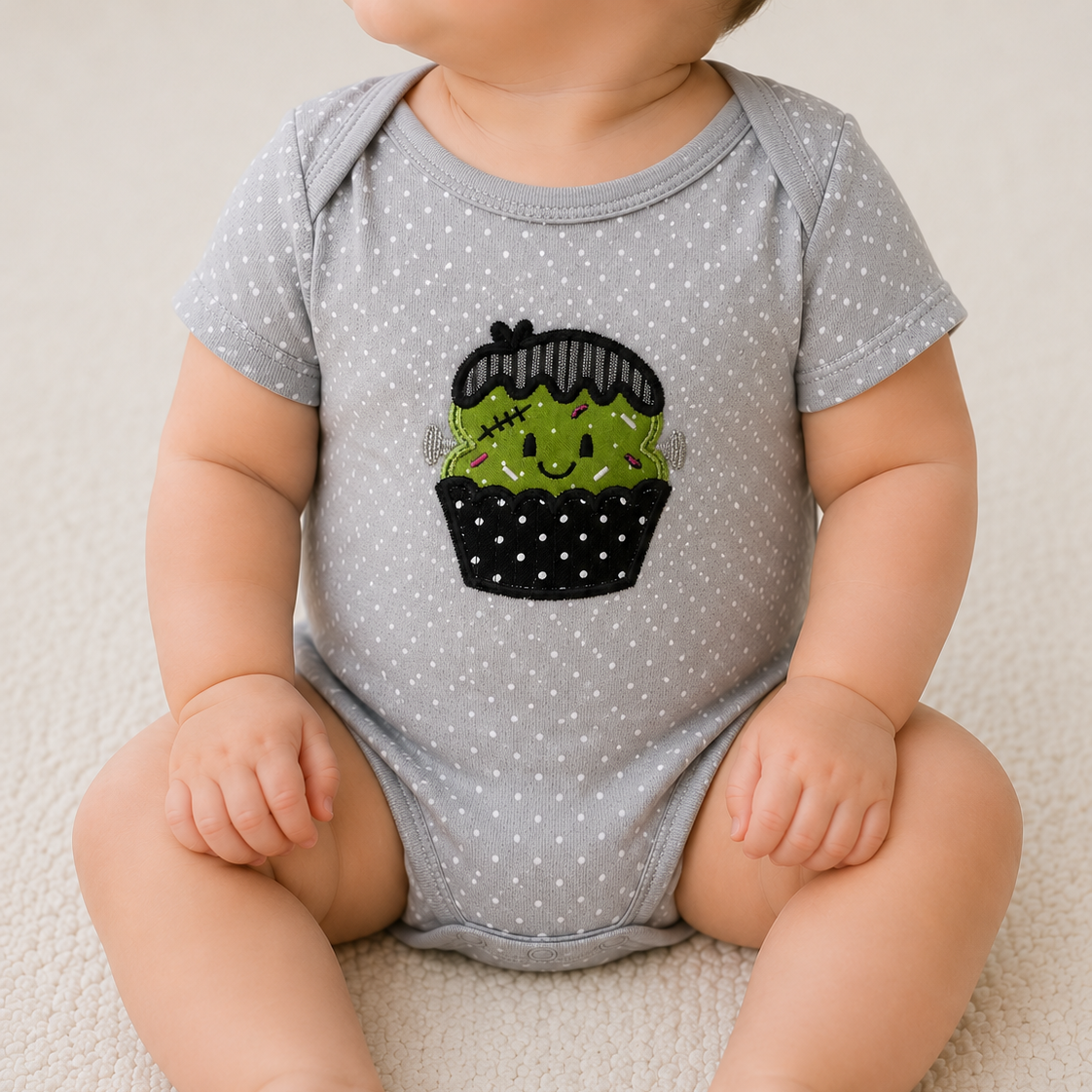Baby wearing a gray onesie with a black and green cactus design on a white background