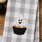 Checkered towel with a ghost-themed cupcake design on a wooden surface.