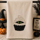 Beige towel with a Halloween-themed cupcake design on a kitchen counter with decorative items.