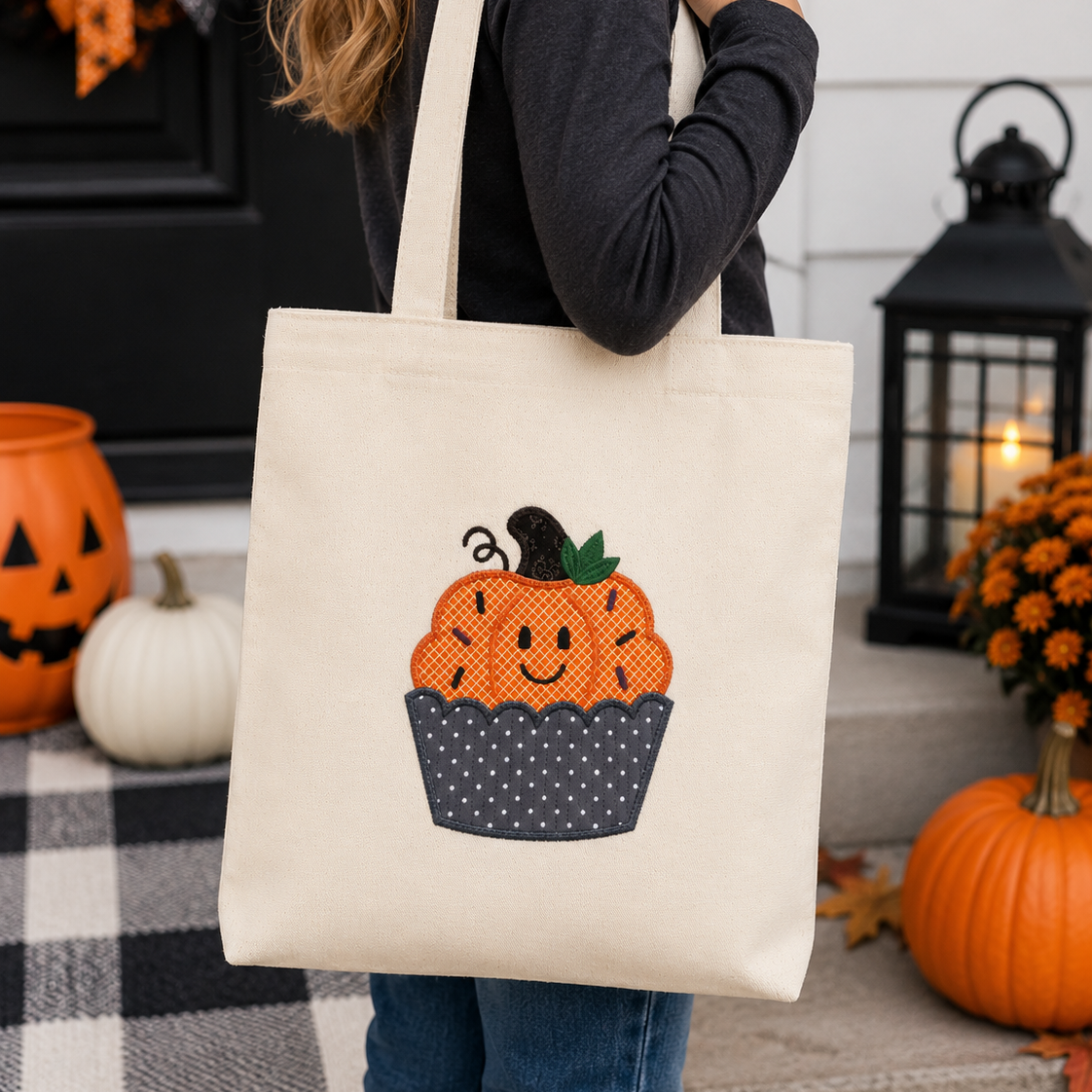 Person holding a tote bag with a pumpkin design on a Halloween-themed porch.