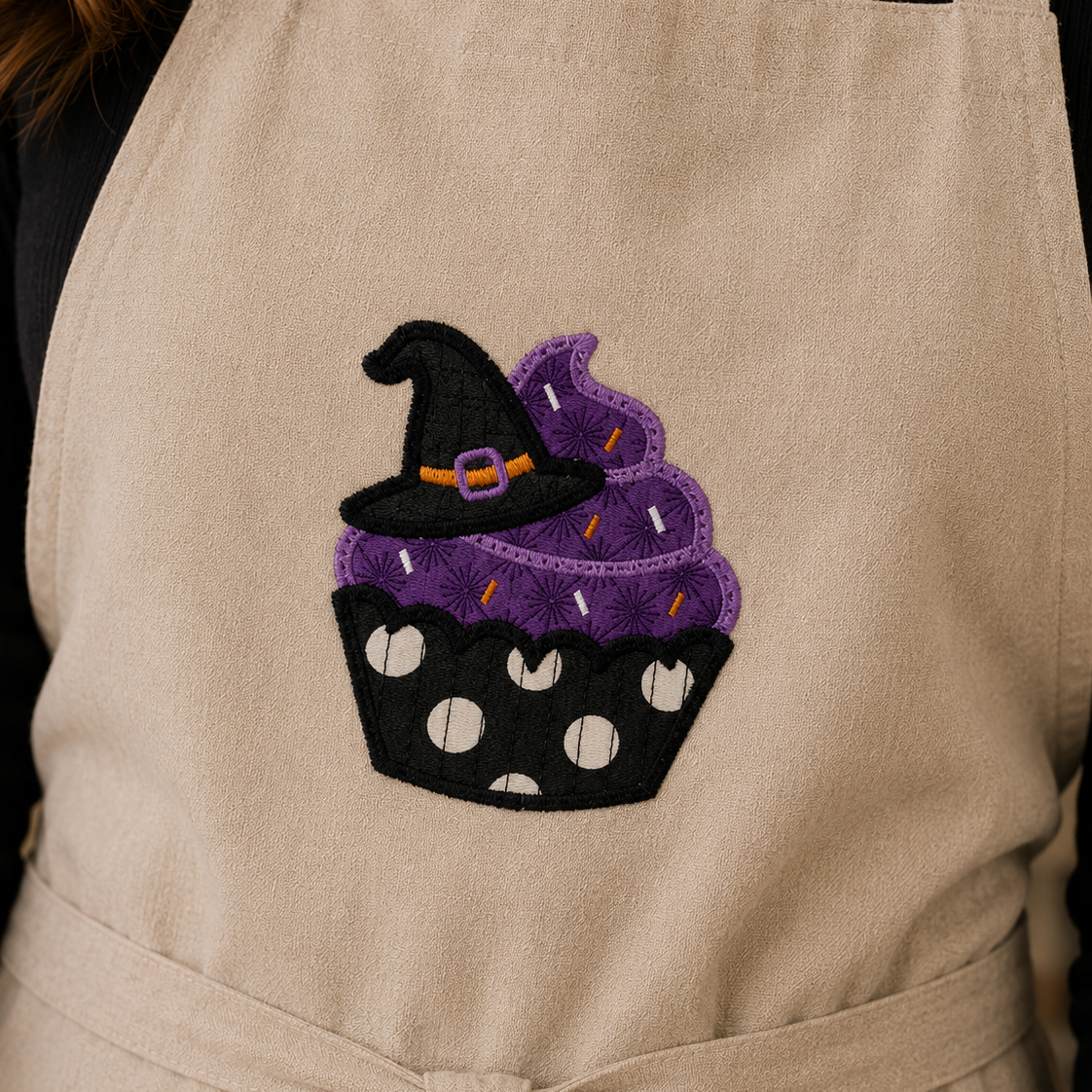 Beige apron with a Halloween-themed cupcake design featuring a witch's hat.
