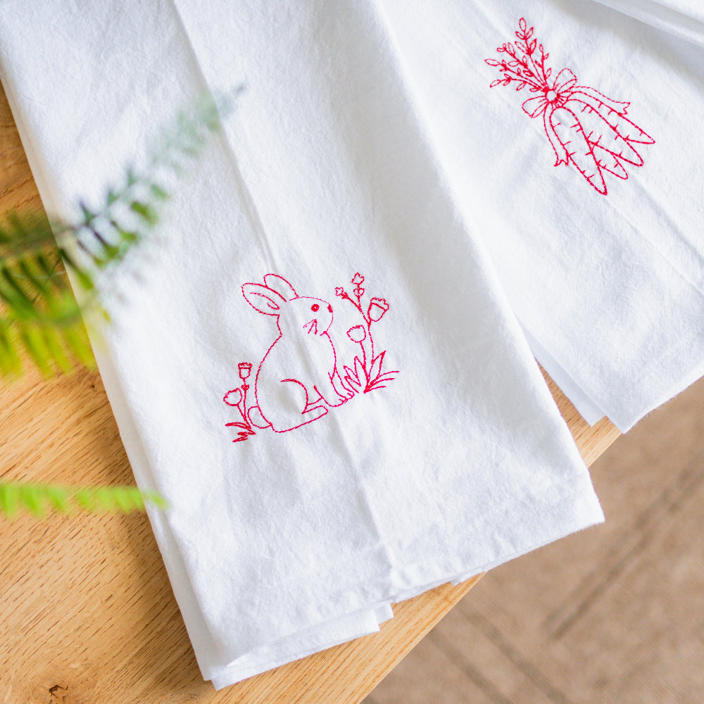 White towels with red embroidered bunny designs on a wooden surface