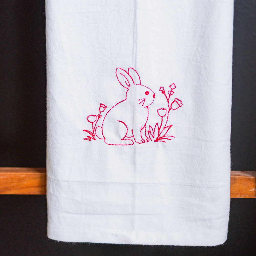 White towel with red embroidered bunny design on a wooden rack against a black background