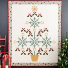 Christmas-themed quilt with tree design on a dark wall with decorative elements.