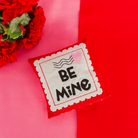 Red carnations with a 'BE MINE' card on a pink background