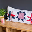 Quilted pillow with star patterns on a wooden surface against a dark wall.