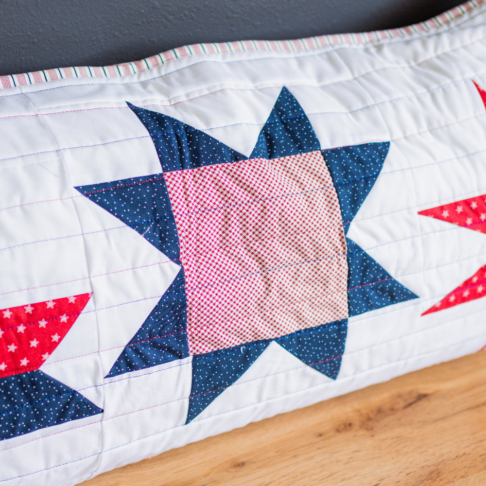 Quilt with star patterns in red, white, and blue on a wooden surface.