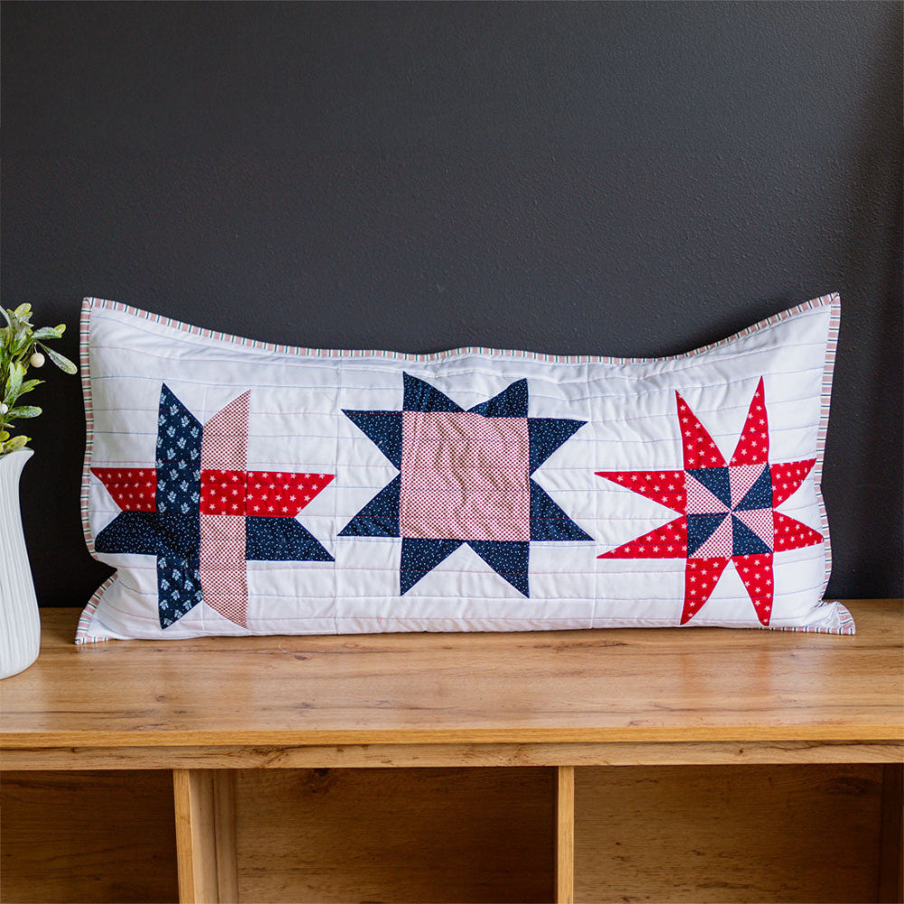 Quilted pillow with star patterns on a wooden surface against a dark background