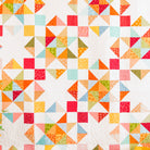 A colorful patchwork quilt hanging on a dark gray wall, featuring a geometric starburst pattern with triangles and squares in orange, red, yellow, green, and light blue on a white background.