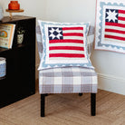 Chair with a decorative pillow featuring an American flag design, in a room with a bookshelf and wall art.