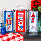 Decorative wall hangings with patriotic designs on a stand against a white wall.