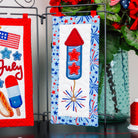 Decorative items with July 4th theme including a rocket, stars, and fireworks on a stand.