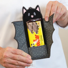 Black cat-shaped pouch with a polka dot pattern holding a Nestle Toblerone chocolate bar.