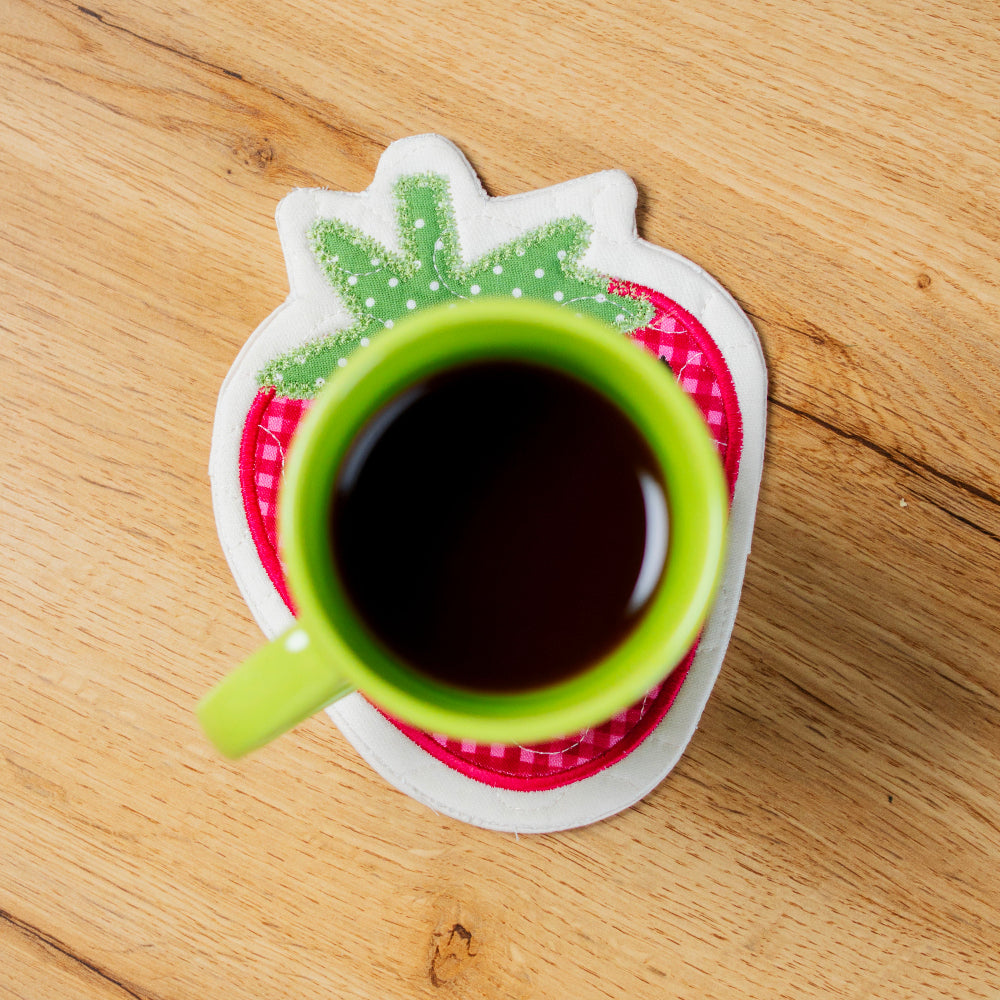 Green mug with black liquid on a matching coaster with a leaf design on a wooden surface