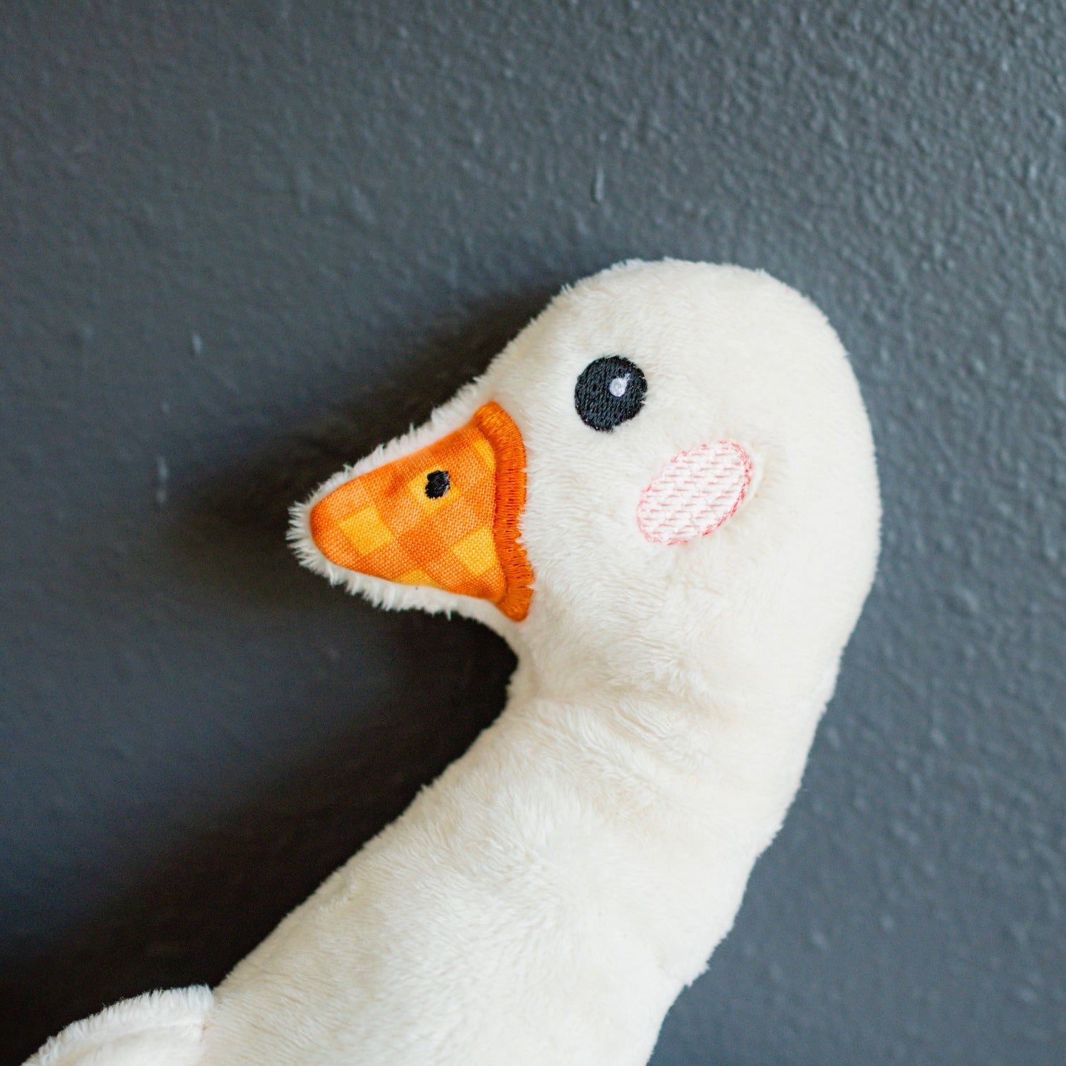 White plush duck toy with orange beak against a dark background