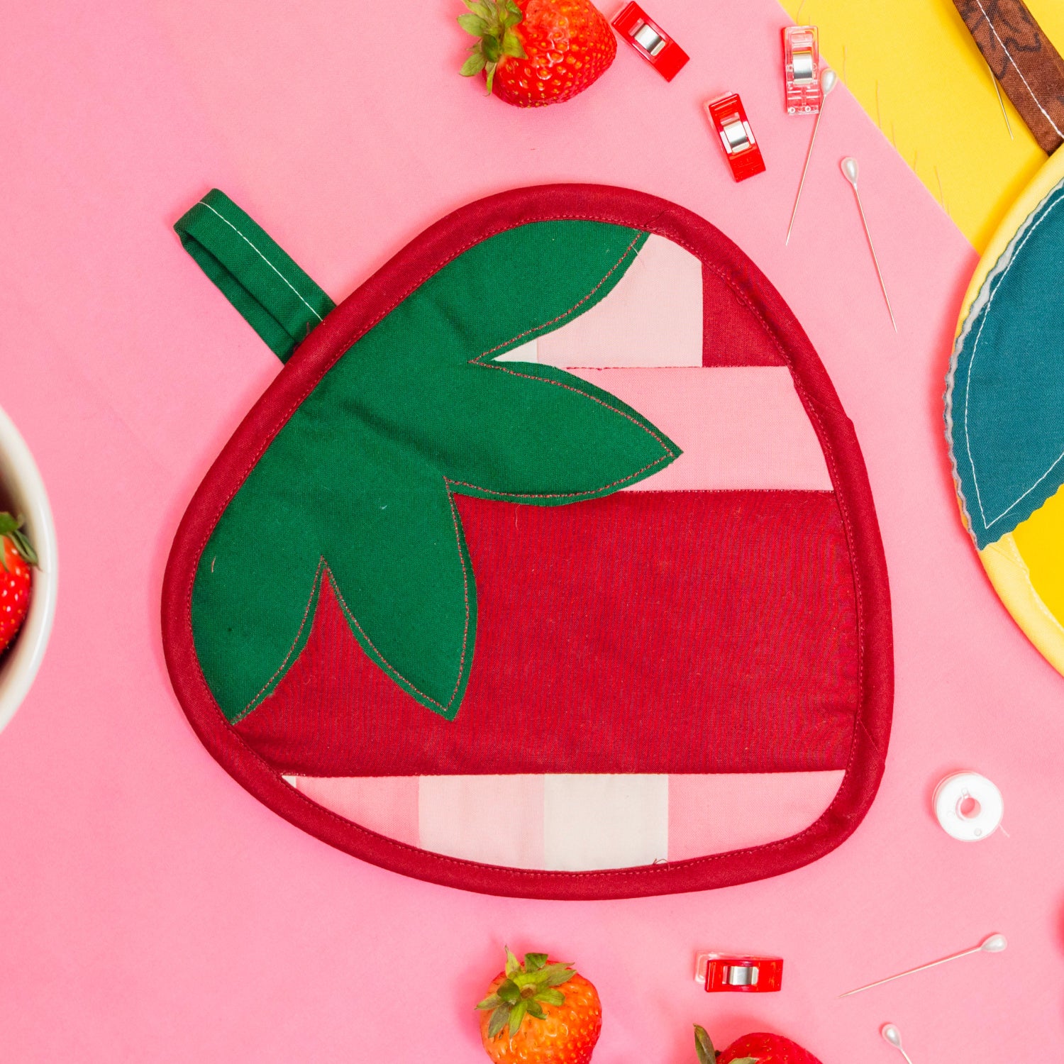 Strawberry-shaped pot holder on a pink background with strawberry decorations