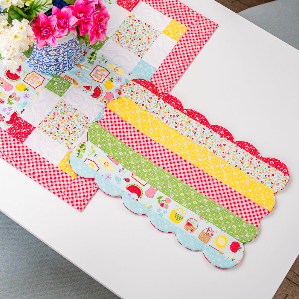 Colorful patchwork table runner on a white surface with flowers in the background