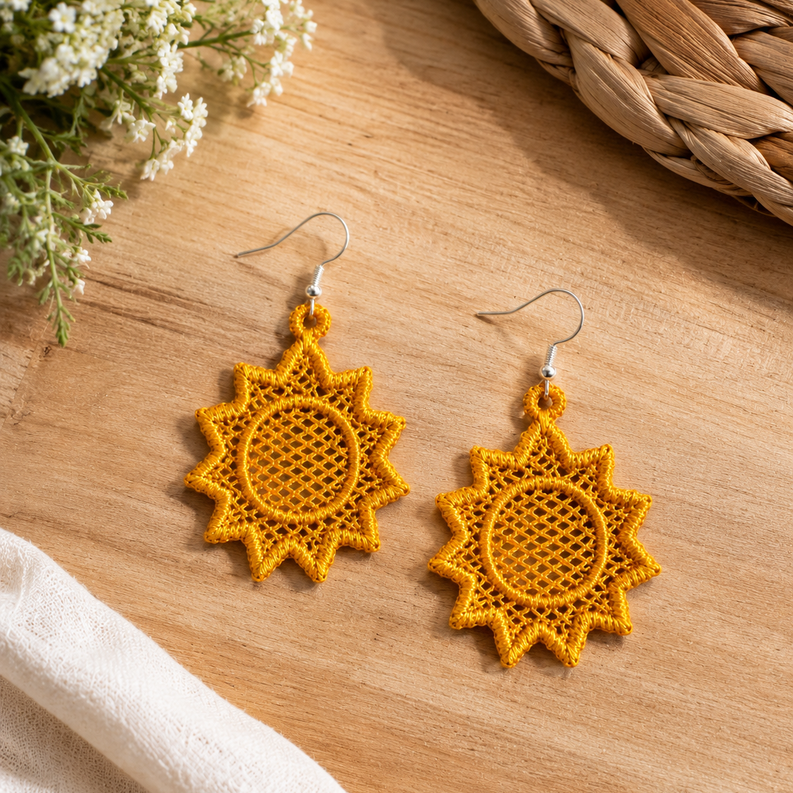 Yellow sun-shaped earrings on a wooden surface with flowers and fabric.