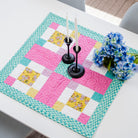 Colorful quilted table runner on a white table with candles and flowers.