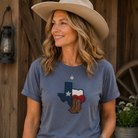 Woman wearing a blue t-shirt with a Texas design, standing in front of a wooden wall.