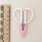 Pink scissors with white handles next to a wooden ruler on a beige background