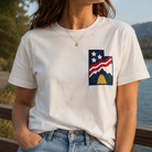 Person wearing a white t-shirt with a graphic design by a lake