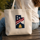 Person holding a tote bag with a design of a mountain, stars, and stripes.