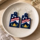 Embroidered earrings with American flag design on a ceramic plate.
