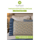 Sewing pattern cover for 'Vintage Ruffled Pillowcase' by my girlfriend's quilt shoppe, showing a finished quilted pillowcase with a blue ruffled border and a yellow floral pattern on a cream background, styled on a bed.
