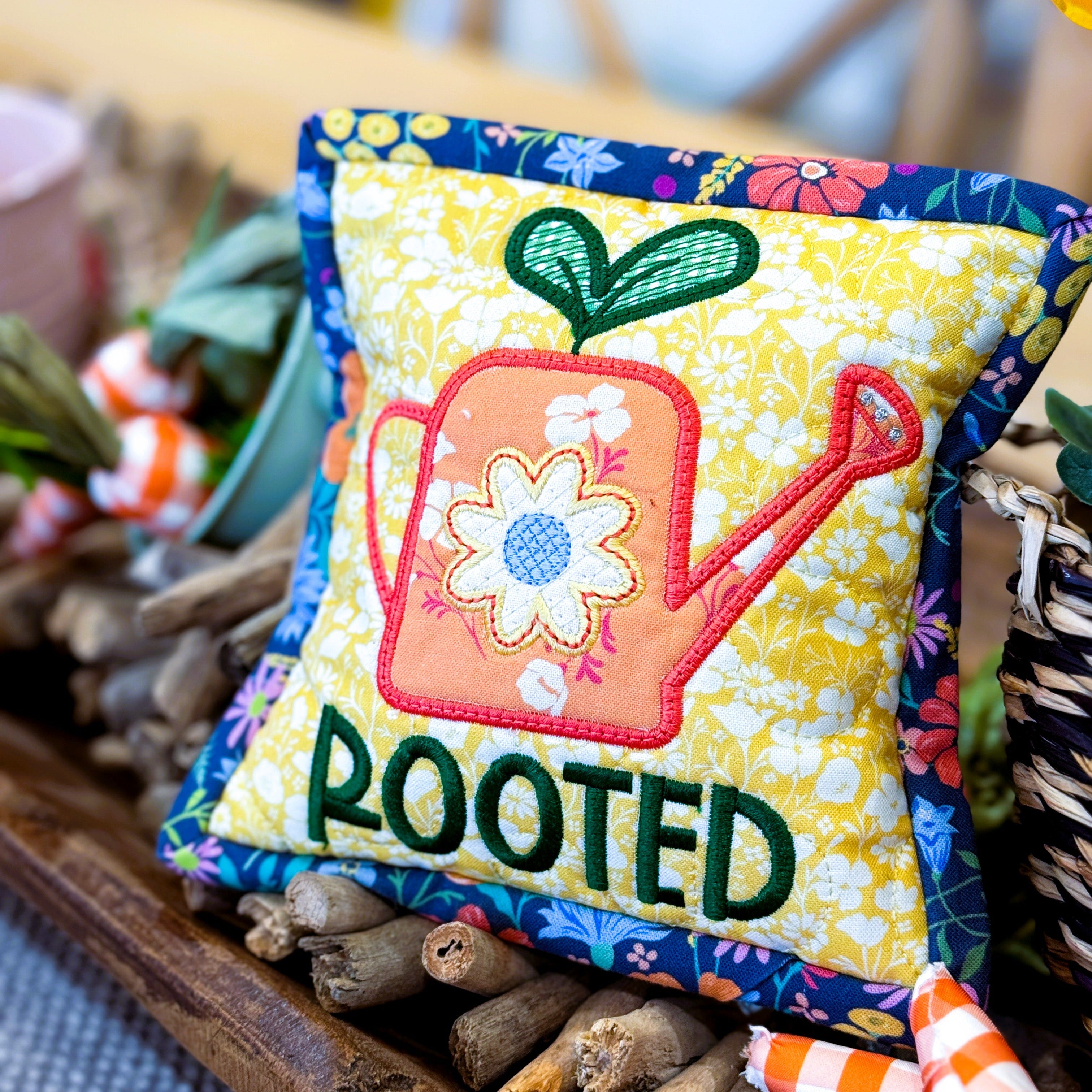 Decorative pillow with 'ROOTED' text and gardening-themed design on a table.