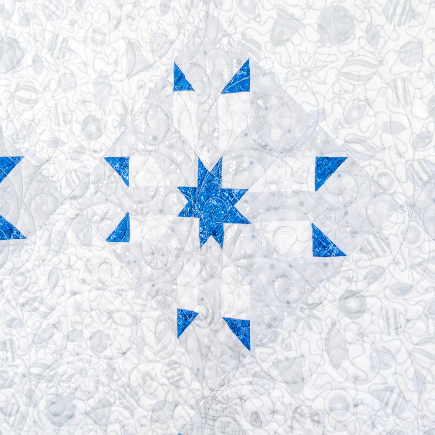 A square textile product, likely a quilt or patchwork fabric, featuring a white background with a distressed, textured blue pattern of geometric shapes including stars and triangles.