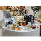 A styled Halloween-themed table display with candles, candy bowls, plates, decorative signs, pumpkins, and assorted party decor in a home interior setting.