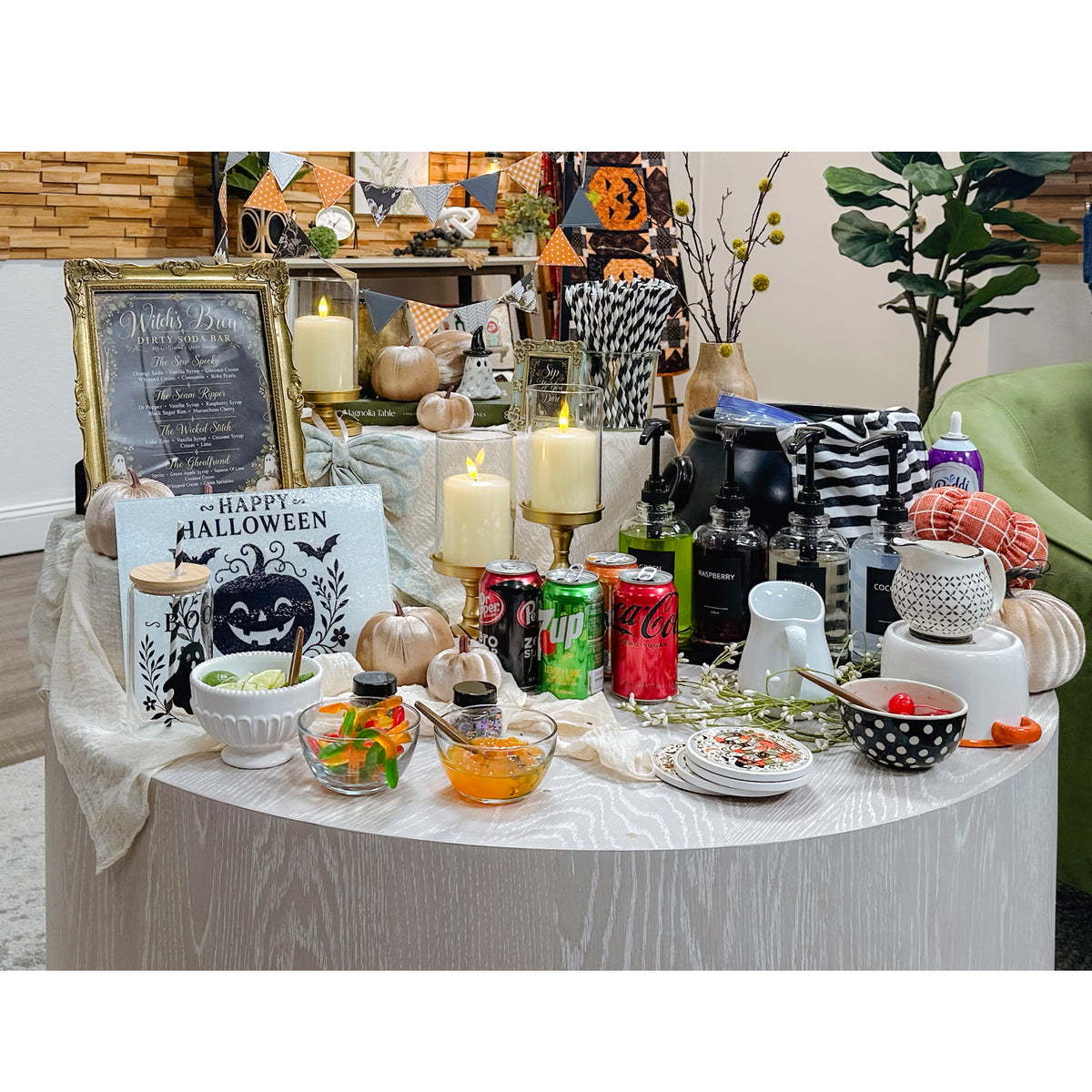 A styled Halloween-themed table display with candles, candy bowls, plates, decorative signs, pumpkins, and assorted party decor in a home interior setting.